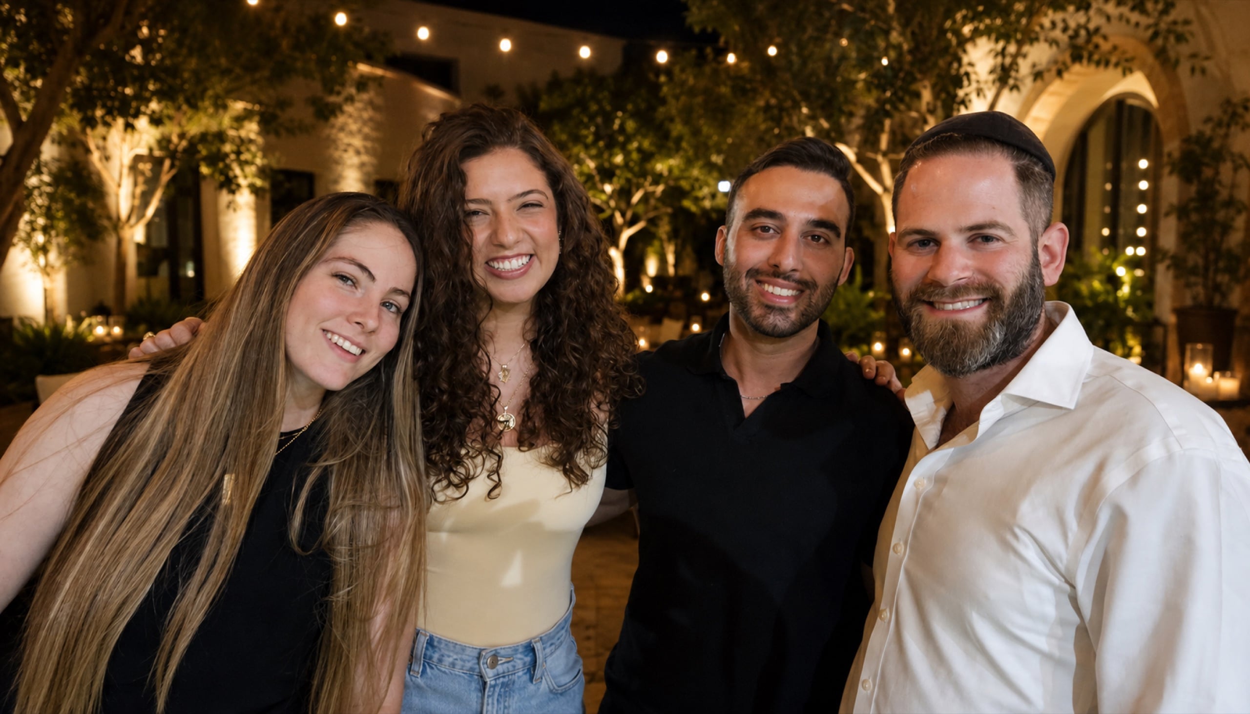 Four friends smiling in a courtyard under string lights